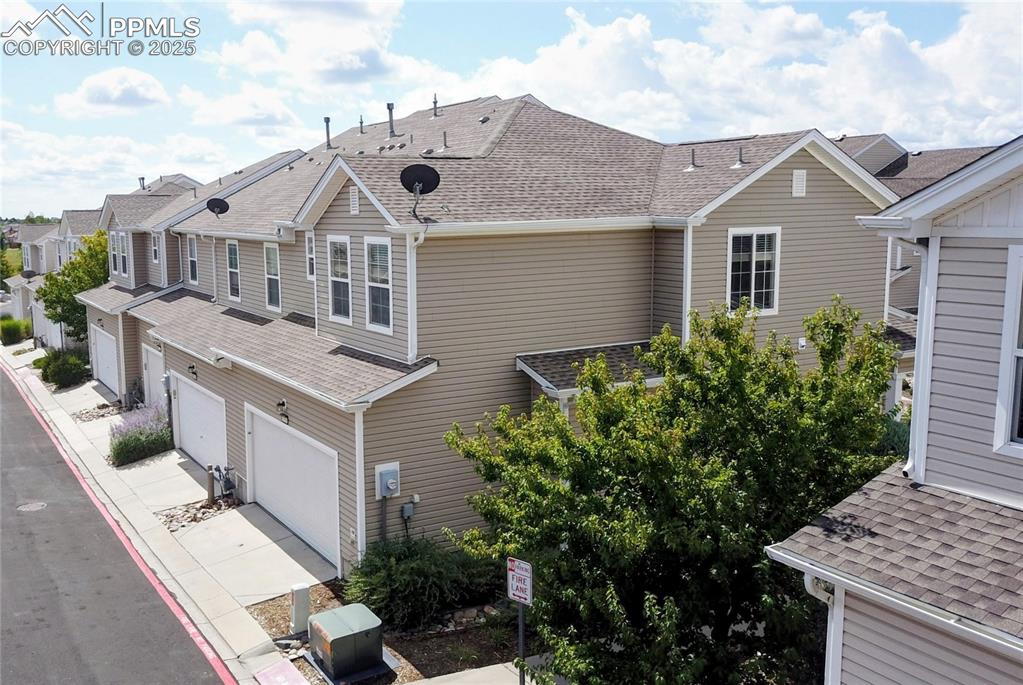 View of side of home featuring roof with shingles, driveway, a garage, and a residential view