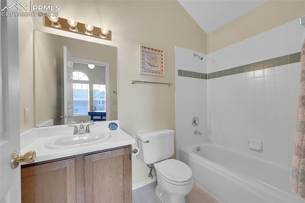 Full adjoining bathroom featuring skylight, vaulted ceiling, tile floor & surround