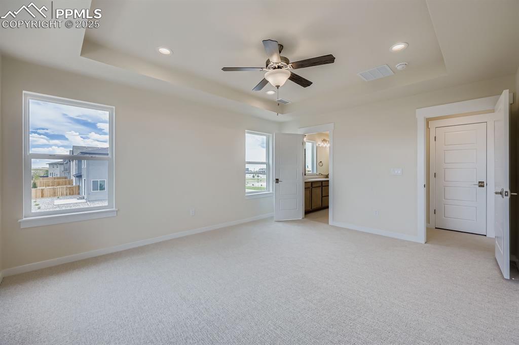 Unfurnished bedroom featuring a raised ceiling, light carpet, recessed lighting, ensuite bathroom, and a ceiling fan
