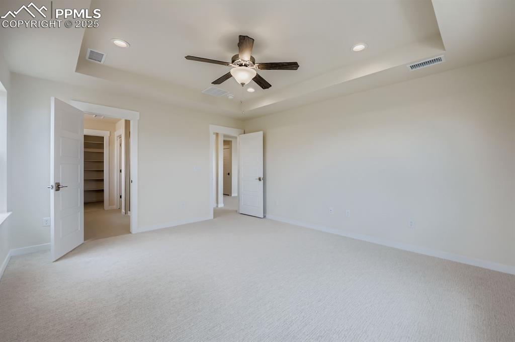 Unfurnished bedroom with a tray ceiling, recessed lighting, light carpet, and ceiling fan