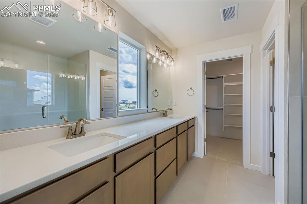 Bathroom featuring a stall shower, double vanity, a spacious closet, and tile patterned floors