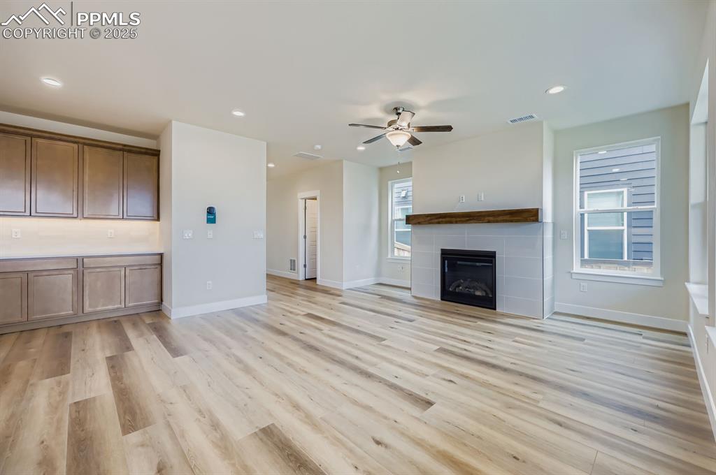 Unfurnished living room featuring a ceiling fan, light wood finished floors, recessed lighting, and a tiled fireplace