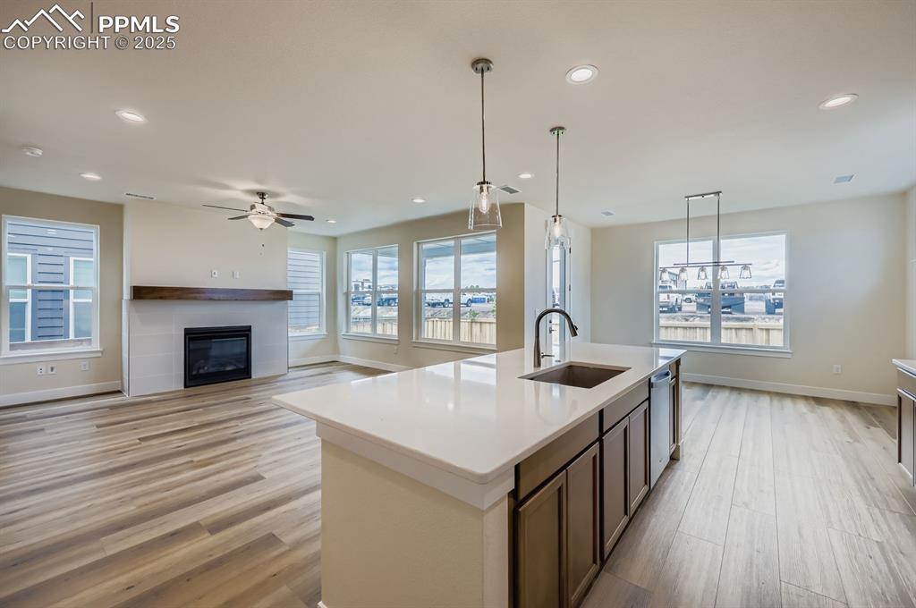 Kitchen featuring light wood-style flooring, recessed lighting, an island with sink, a ceiling fan, and a glass covered fireplace