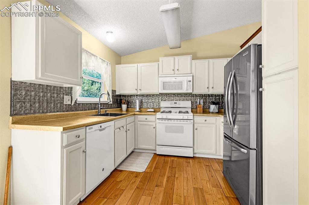Kitchen featuring white appliances, backsplash, light wood-style floors, a textured ceiling, and white cabinetry