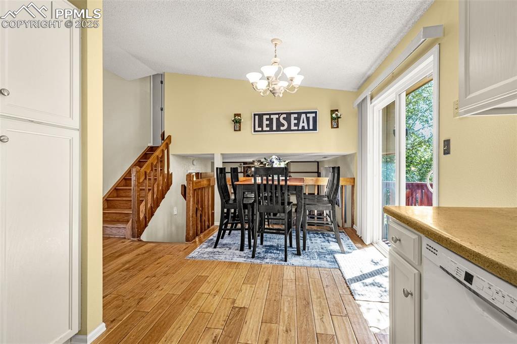 Dining room with vaulted ceiling, light wood-style floors, a chandelier, and a textured ceiling