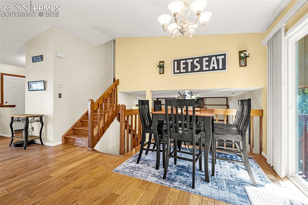 Dining room with a chandelier, light wood-style floors, vaulted ceiling, stairs, and a textured ceiling