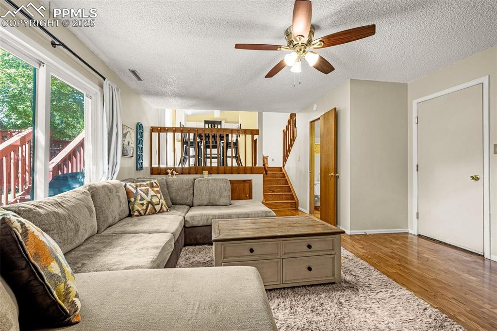Living area with light wood-style flooring, a textured ceiling, stairway, and a ceiling fan