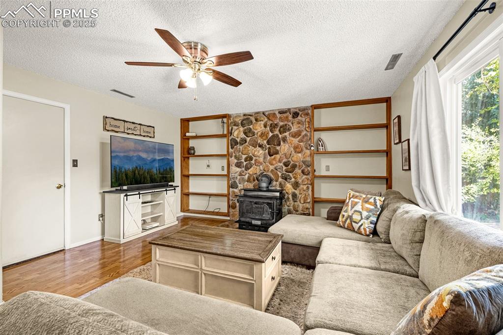 Living area with a wood stove, wood finished floors, a textured ceiling, and ceiling fan