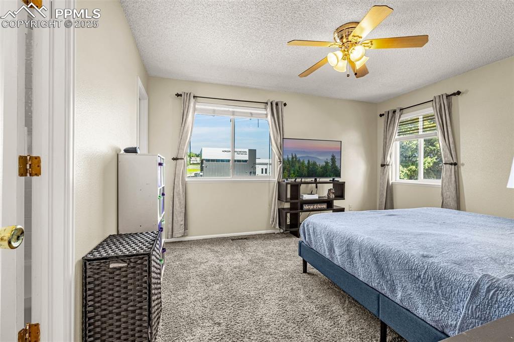 Carpeted bedroom featuring ceiling fan and a textured ceiling