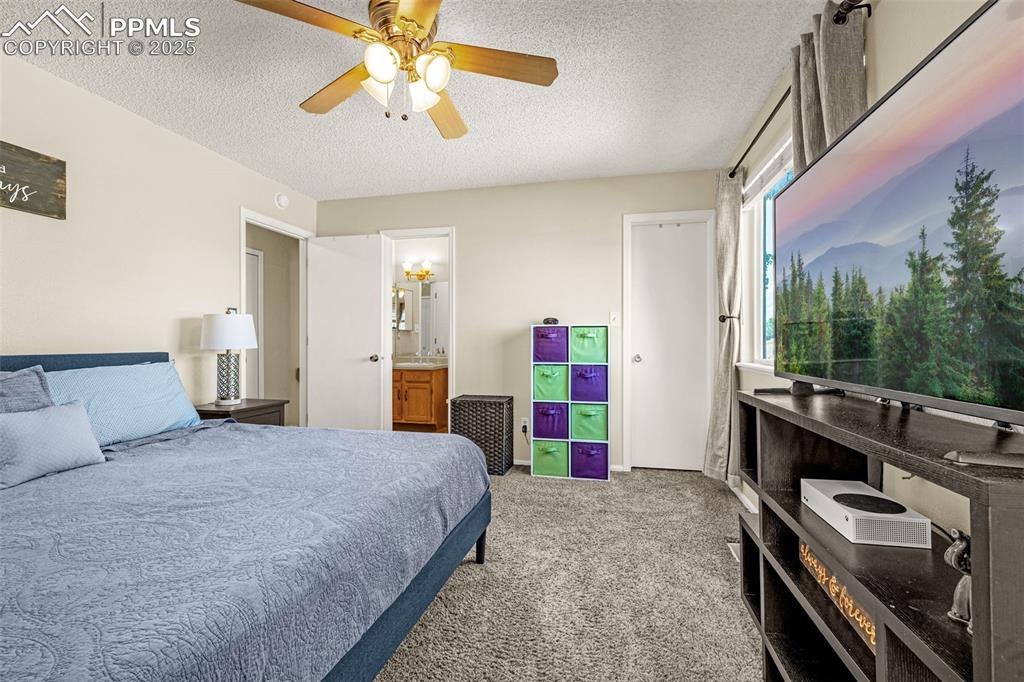 Bedroom with a textured ceiling, light colored carpet, a ceiling fan, and connected bathroom