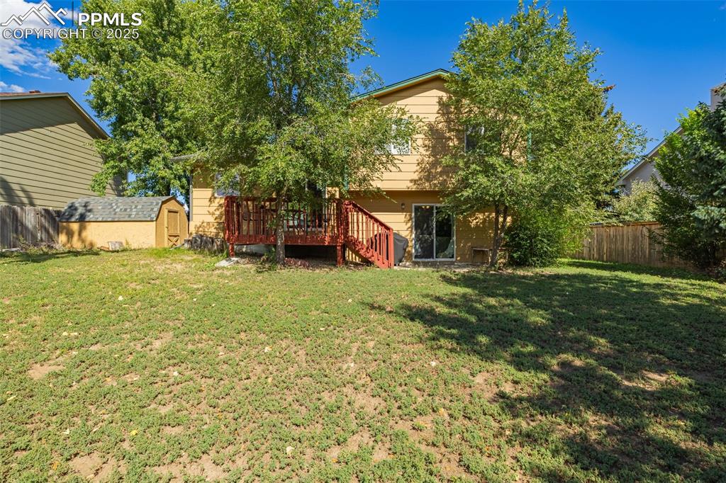 Fenced backyard with a storage unit, a wooden deck, and stairs