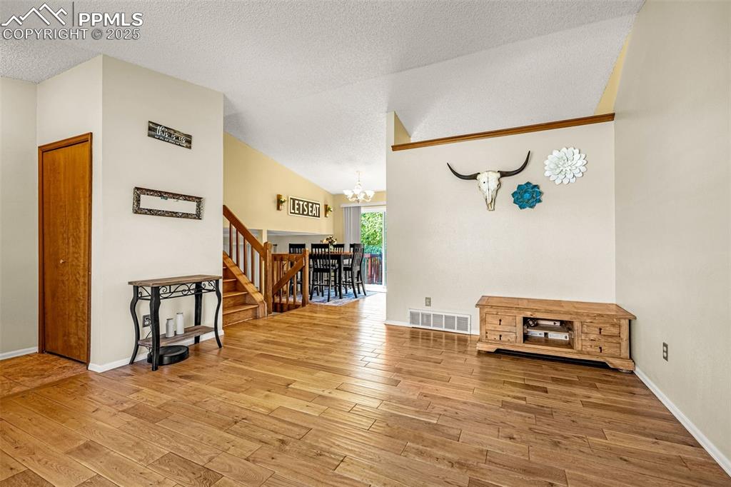 Living room with a chandelier, a textured ceiling, stairway, light wood-style floors, and lofted ceiling