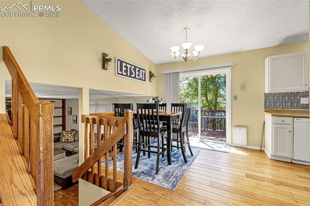 Dining space with a textured ceiling, light wood finished floors, a chandelier, and vaulted ceiling