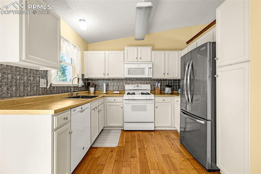 Kitchen featuring white appliances, backsplash, light wood-style flooring, white cabinetry, and a textured ceiling