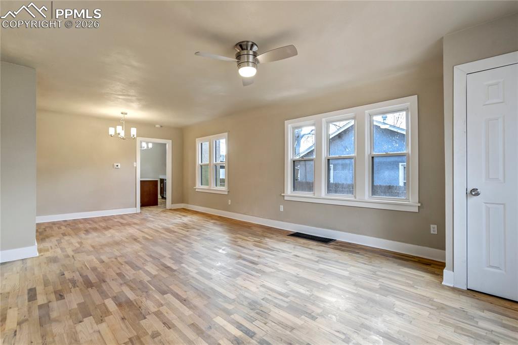 Bright living room with wood floors, ceiling fan, chandelier, and abundant natural light.