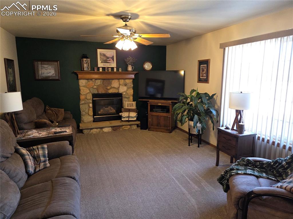 Carpeted living room with a ceiling fan and a stone fireplace