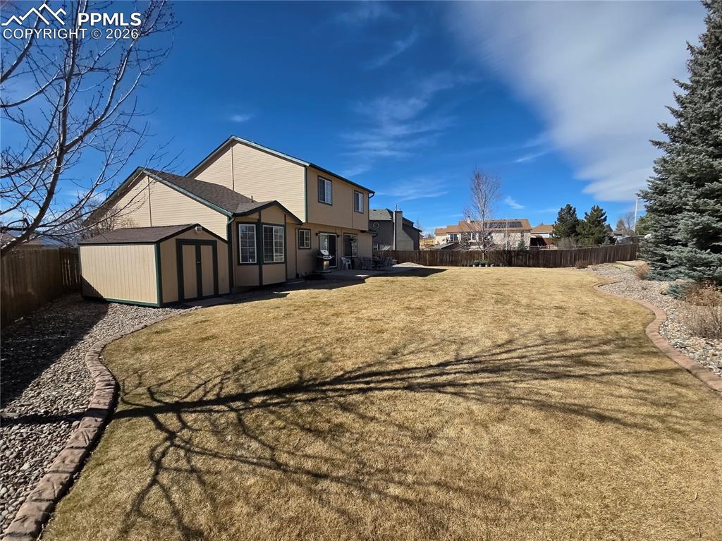 Rear view of property with a storage unit and a fenced backyard