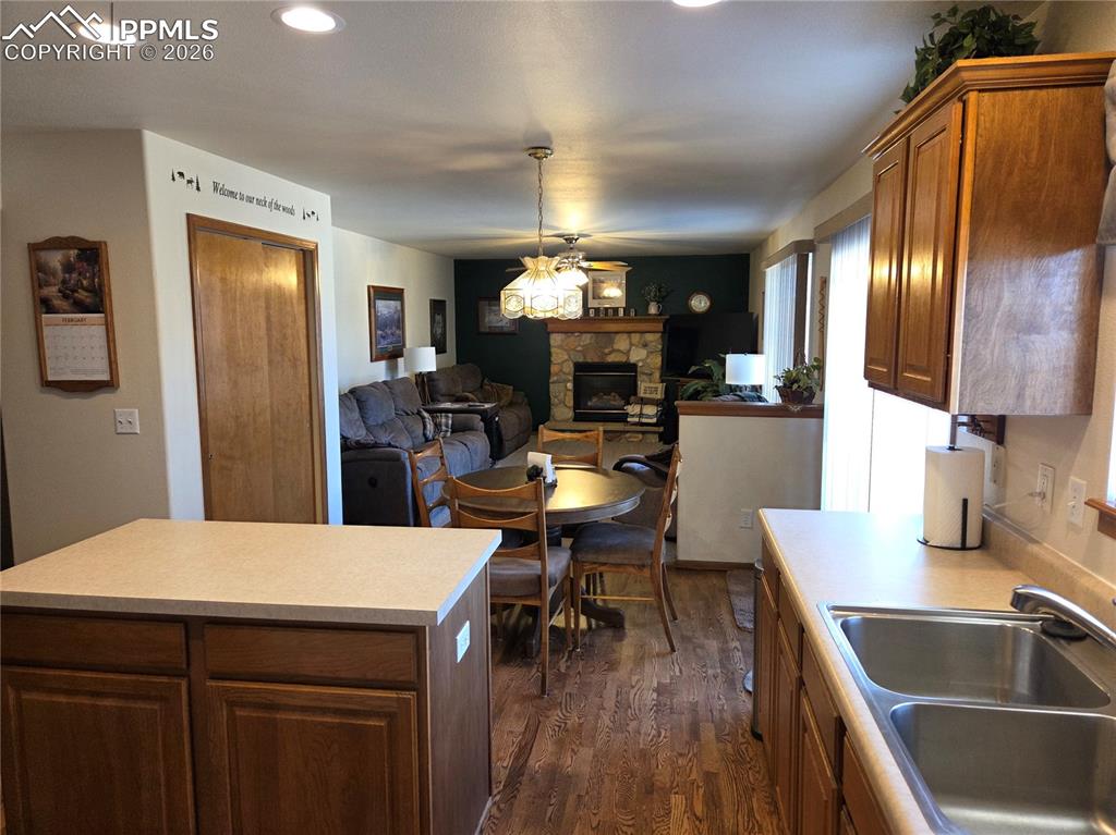 Kitchen with open floor plan, light countertops, dark wood-type flooring, wood finish cabinets, and a stone fireplace