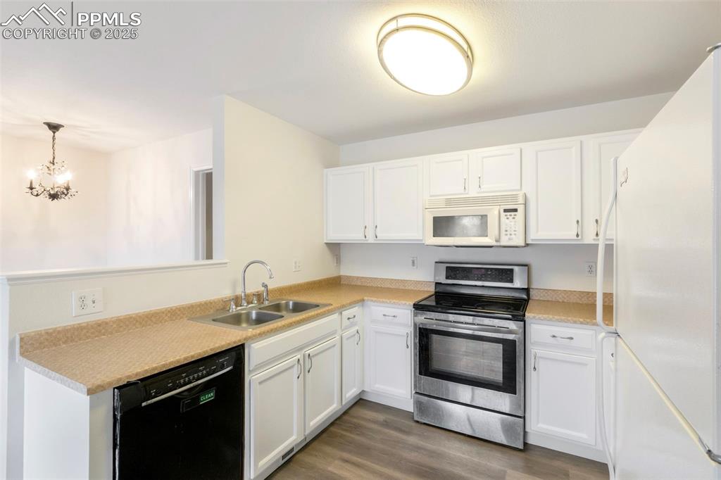 Kitchen with white appliances, white cabinetry, light countertops, dark wood-style flooring, and decorative light fixtures