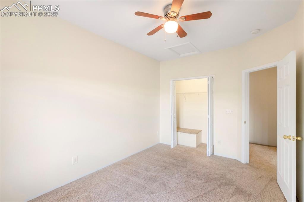 Unfurnished bedroom featuring carpet flooring, a spacious closet, attic access, and a ceiling fan
