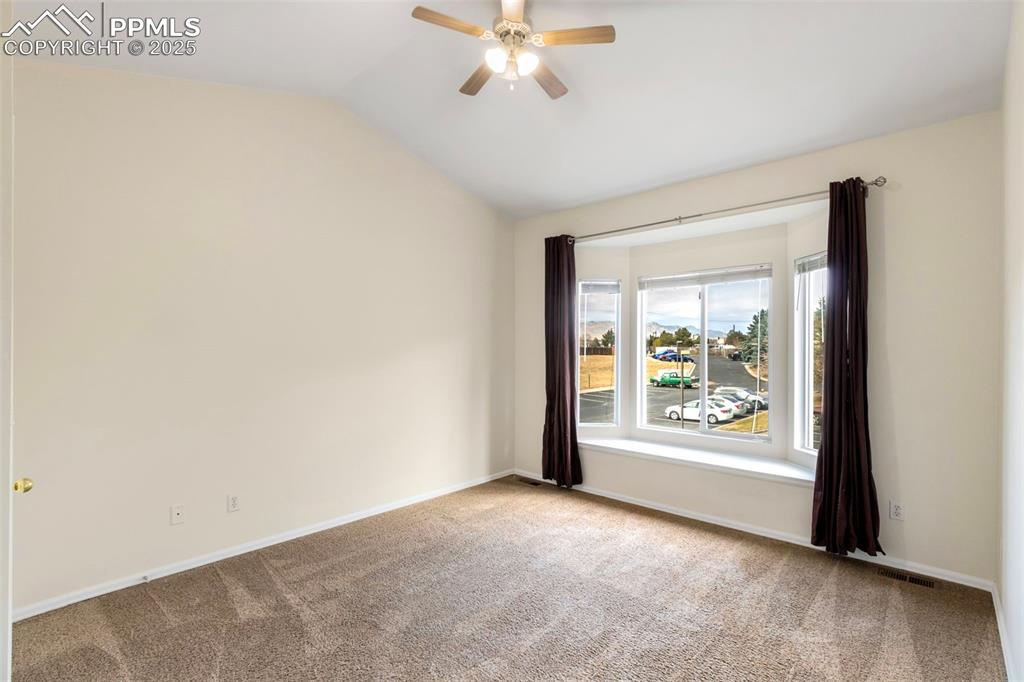 Carpeted empty room with lofted ceiling and ceiling fan
