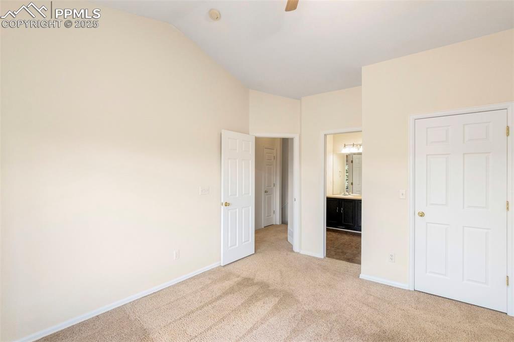 Unfurnished bedroom featuring light carpet, connected bathroom, vaulted ceiling, and a ceiling fan