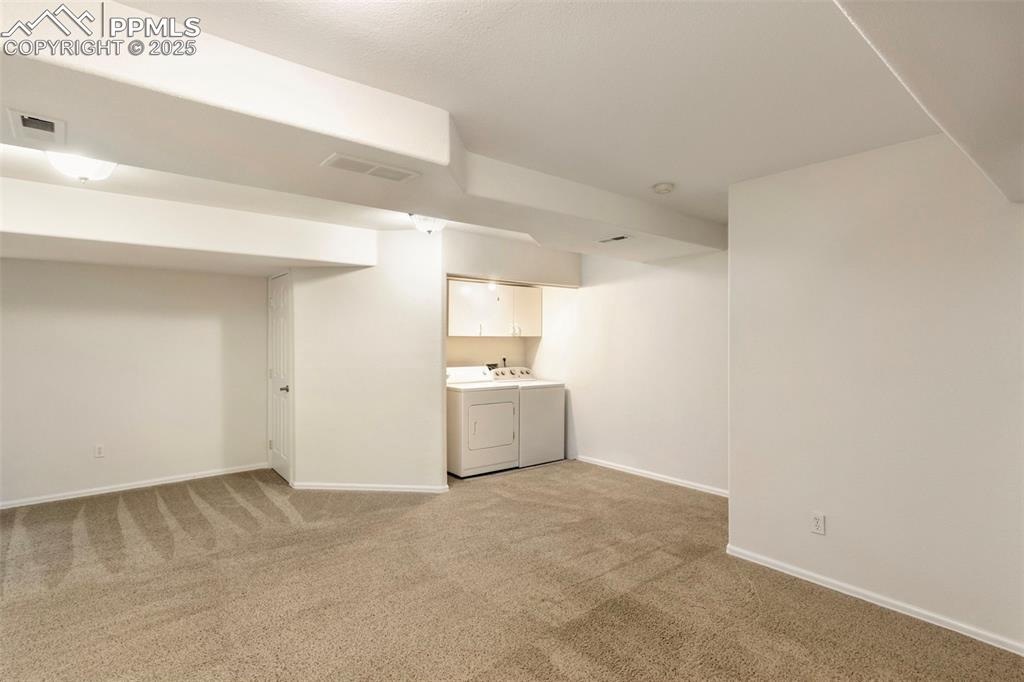 Finished below grade area featuring light colored carpet and washing machine and clothes dryer