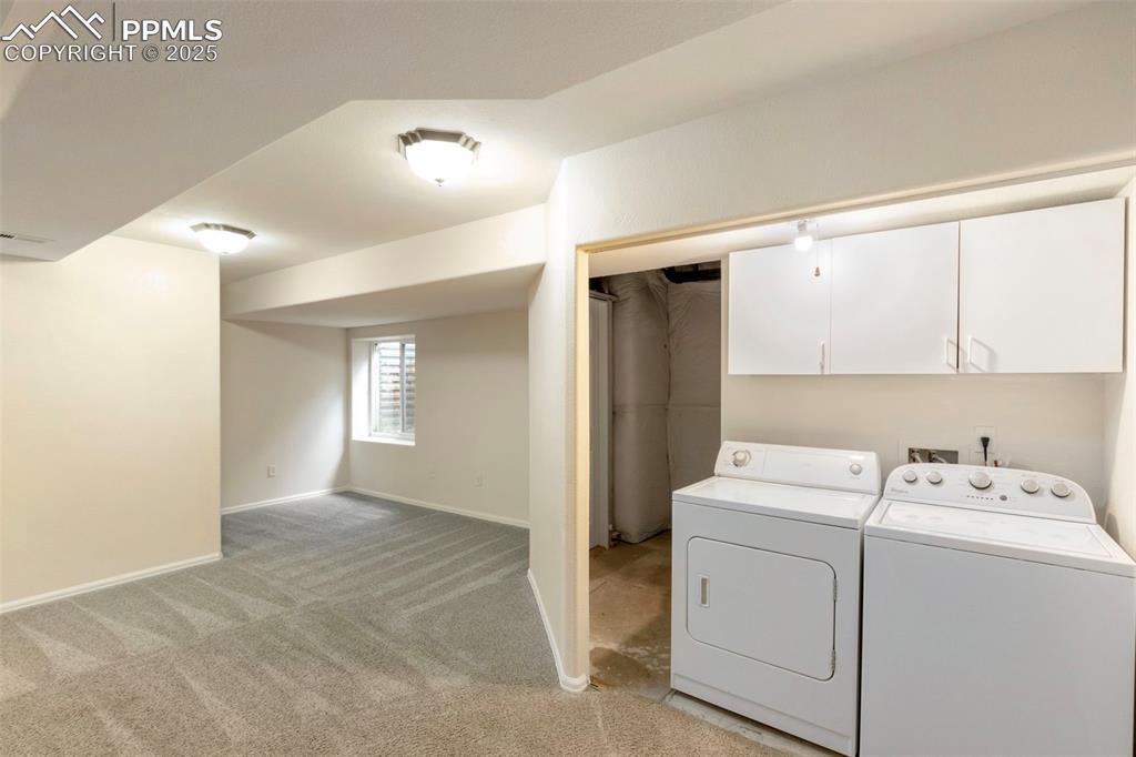 Laundry area featuring light colored carpet, washing machine and dryer, and cabinet space