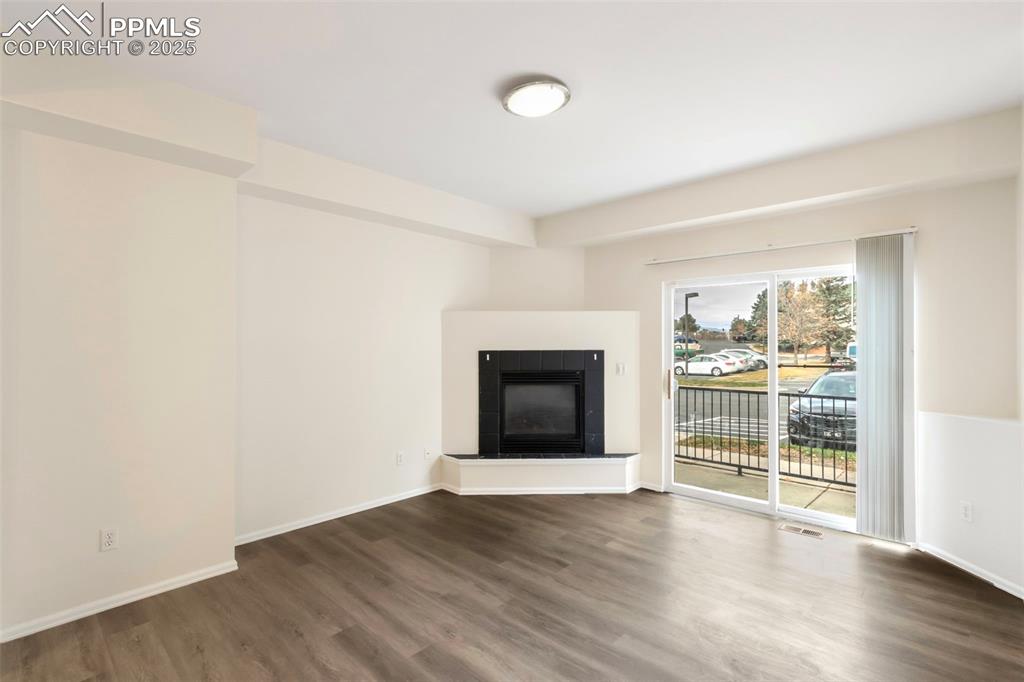 Unfurnished living room with a tiled fireplace and wood finished floors