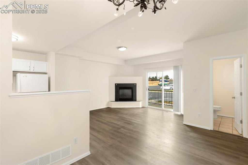 Unfurnished living room with a glass covered fireplace, dark wood finished floors, and a chandelier