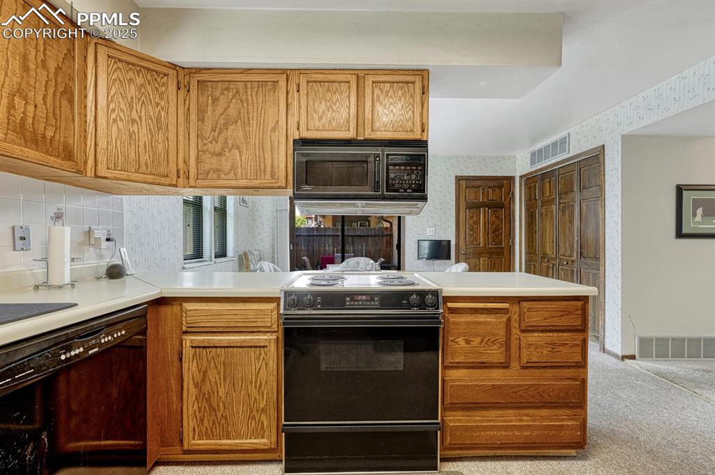 Kitchen with black appliances, a peninsula, light countertops, brown cabinetry, and wallpapered walls