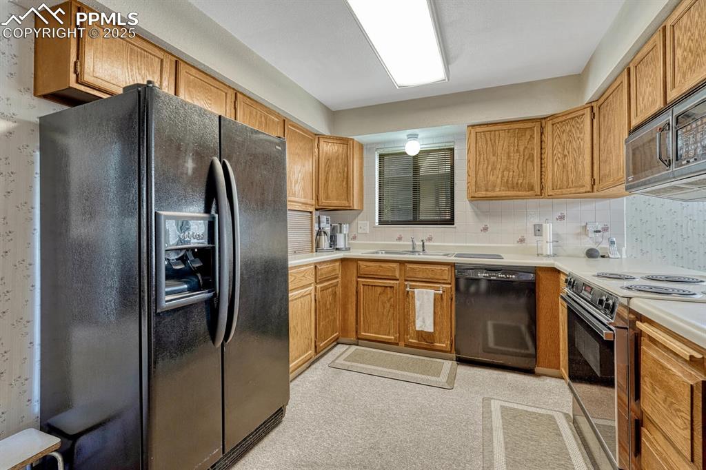 Kitchen with black appliances, brown cabinetry, light countertops, and tasteful backsplash