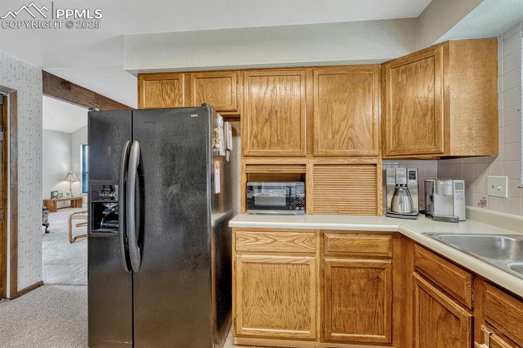 Kitchen featuring black appliances, light colored carpet, light countertops, brown cabinets, and tasteful backsplash