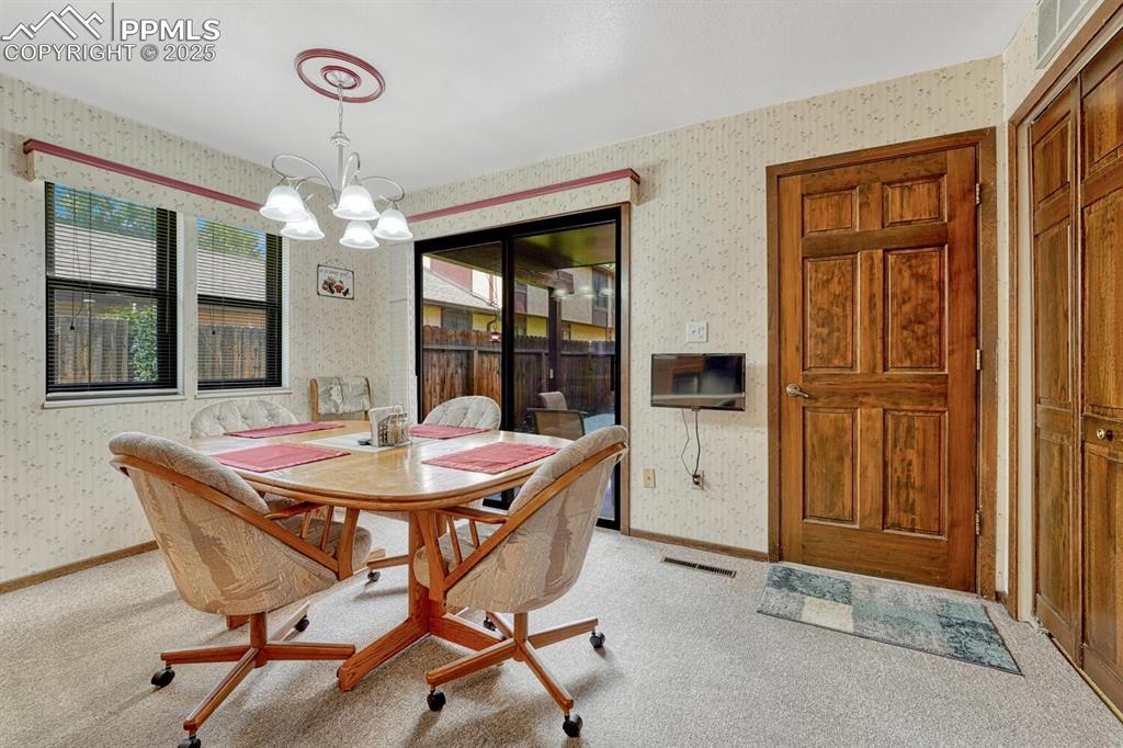 Dining area featuring wallpapered walls, light colored carpet, and a chandelier