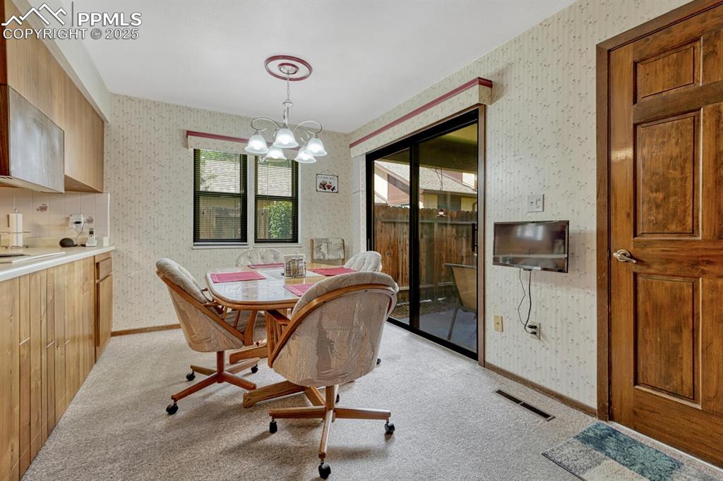 Dining area with light carpet, a chandelier, and wallpapered walls