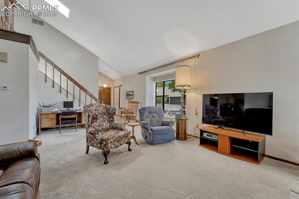 Living room featuring carpet floors, stairway, a textured ceiling, high vaulted ceiling, and a skylight