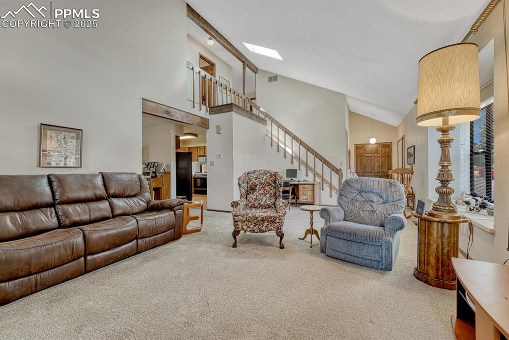 Carpeted living area with high vaulted ceiling and stairway