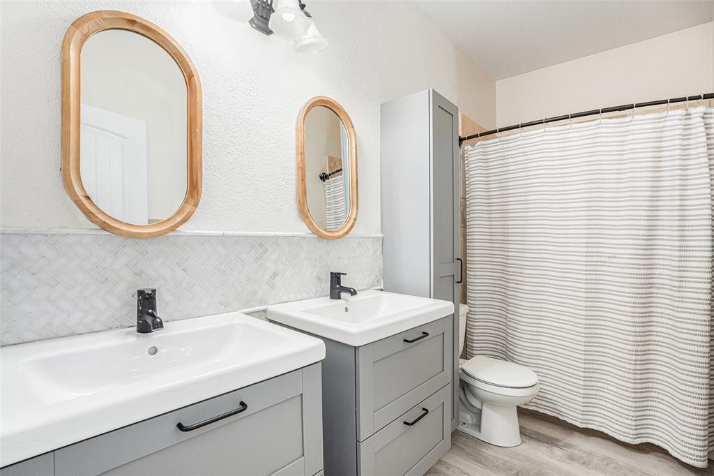 Full bath with two vanities, light wood-style floors, tasteful backsplash, and curtained shower