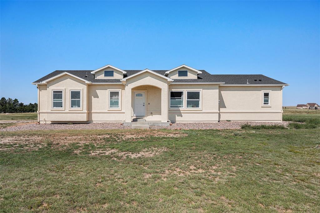View of front of house with a front lawn, roof with shingles, and stucco siding