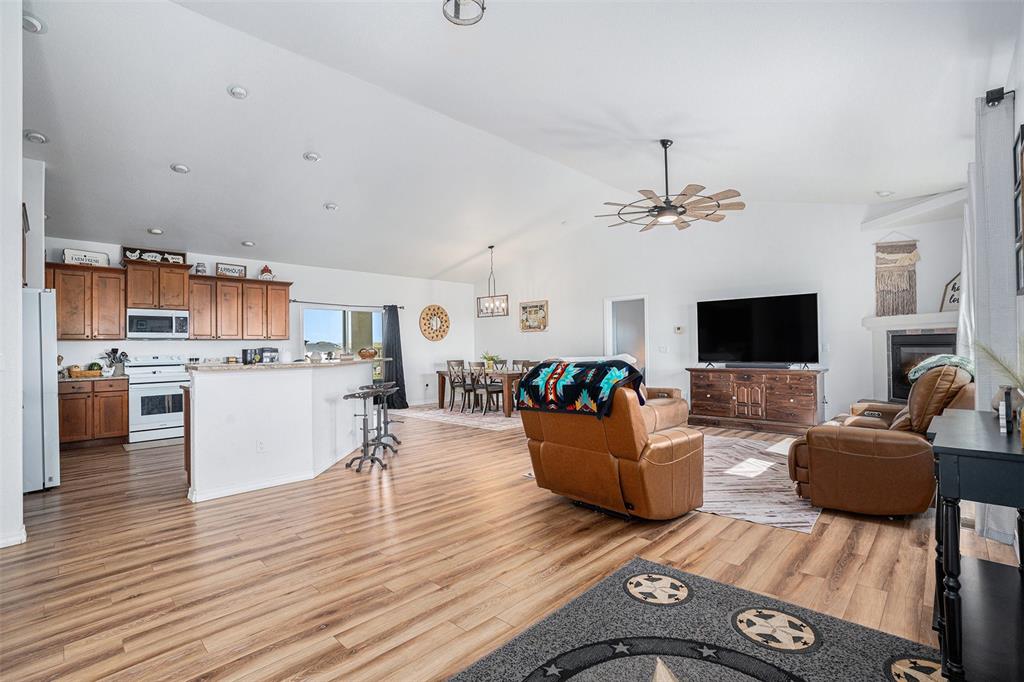 Living room featuring light wood-style floors, high vaulted ceiling, ceiling fan, and a glass covered fireplace