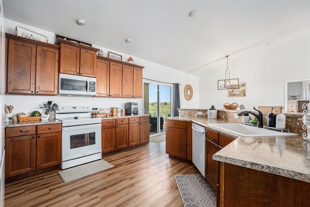 Kitchen featuring lofted ceiling, white appliances, light wood-style flooring, brown cabinetry, and light countertops