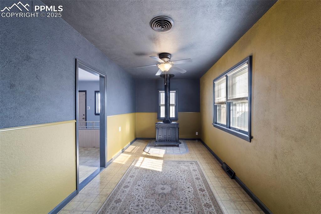 Empty room with a textured wall, a wood stove, ceiling fan, and a textured ceiling