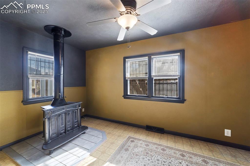 FAmily room with a wood stove, a textured ceiling, light floors, and ceiling fan