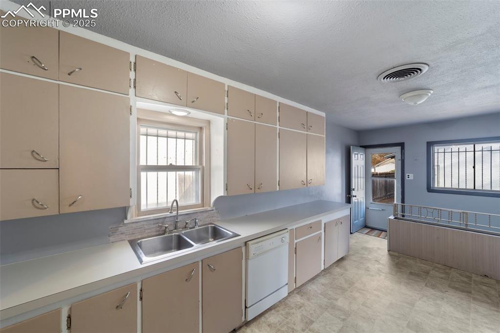 Kitchen featuring light countertops, a textured ceiling, dishwasher, plenty of natural light, and cream cabinets