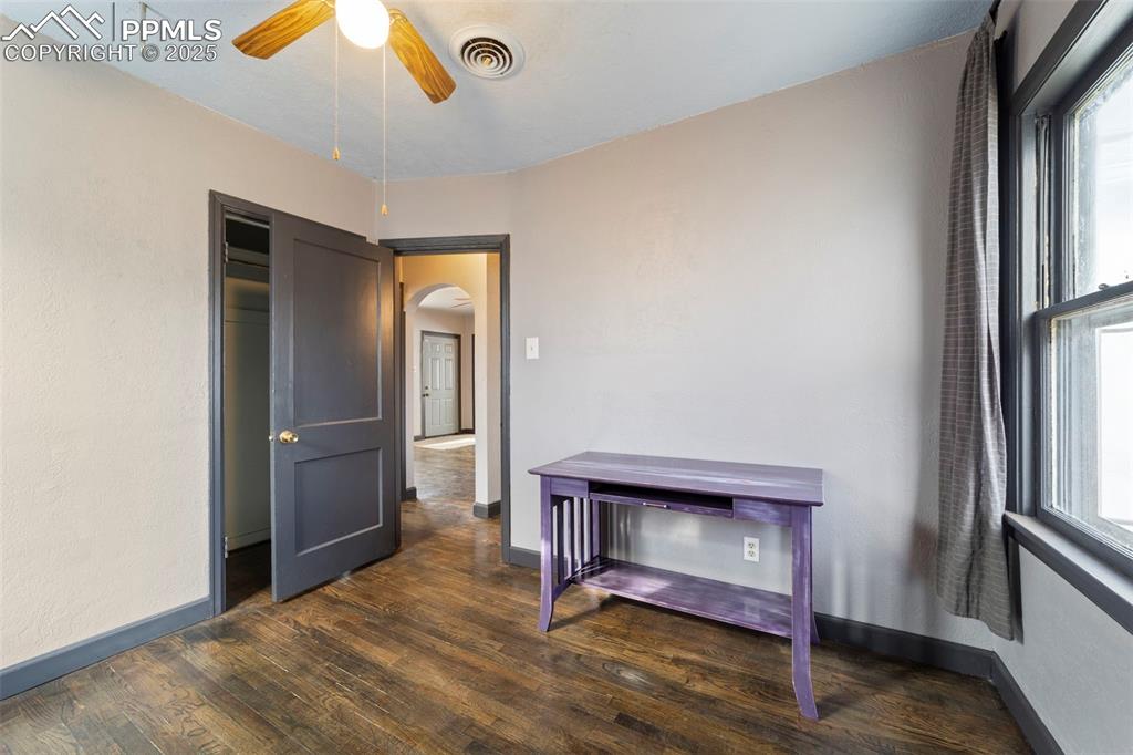 Unfurnished bedroom with dark wood-style flooring, arched walkways, multiple windows, and a ceiling fan