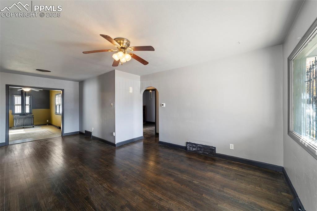Living room featuring arched walkways, a ceiling fan, and dark wood-style flooring