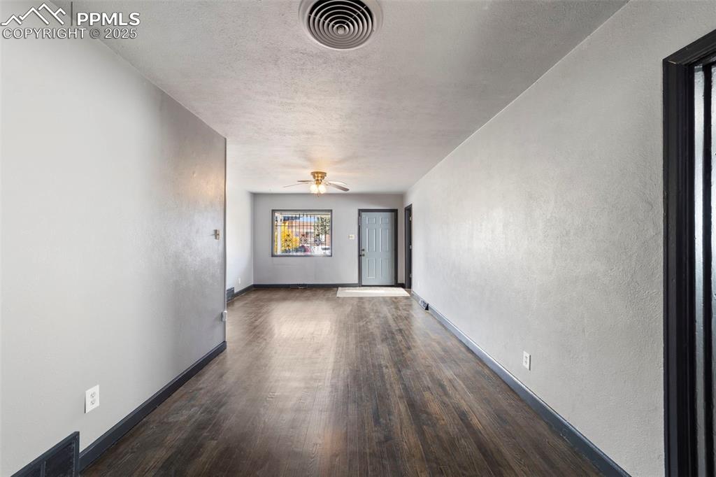 Empty room featuring a textured wall, a textured ceiling, dark wood-style flooring, and ceiling fan