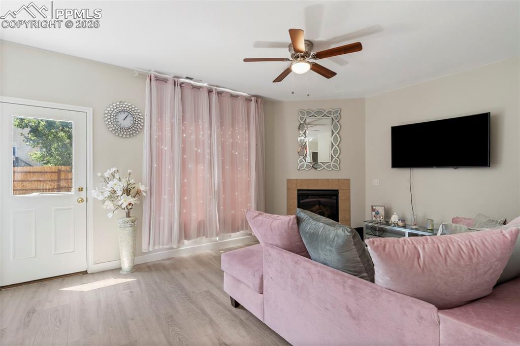 Living room with wood finished floors, a tile fireplace, and a ceiling fan