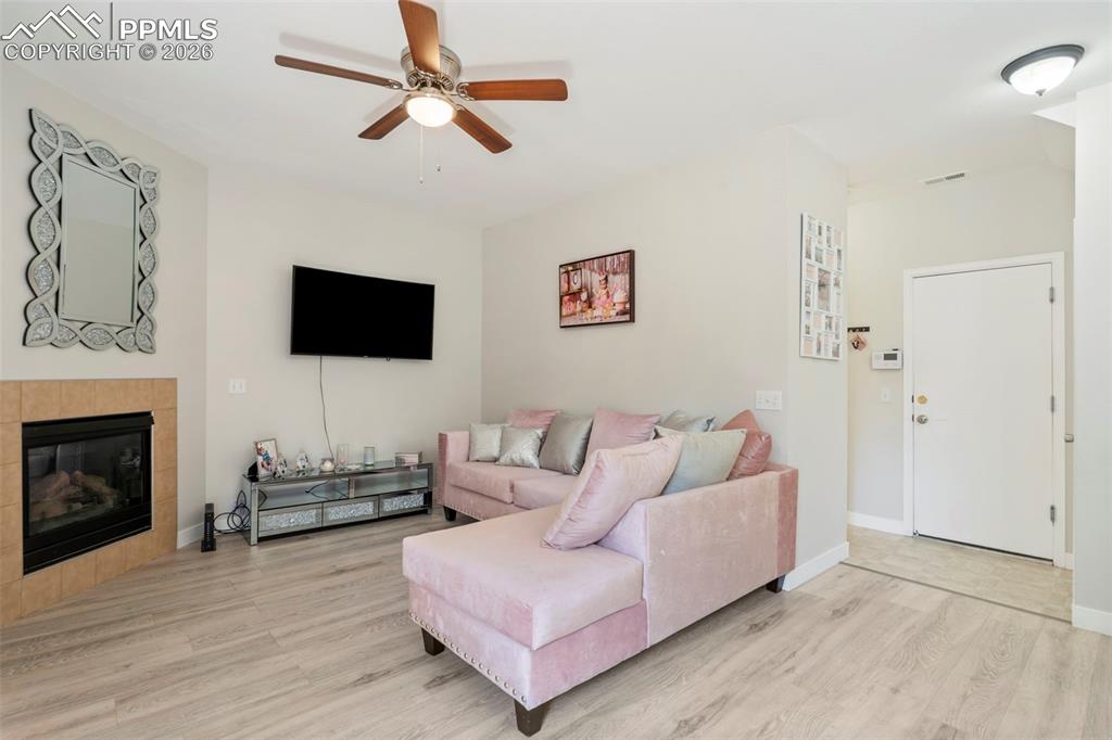 Living room featuring a tile fireplace, ceiling fan, and light wood-type flooring