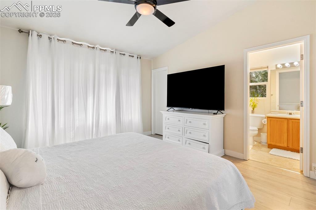 Bedroom featuring lofted ceiling, a ceiling fan, light wood-style floors, and ensuite bath